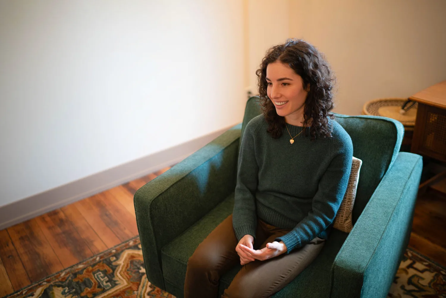 Vanessa seated in a green armchair in her office, hands open, mid-conversation.