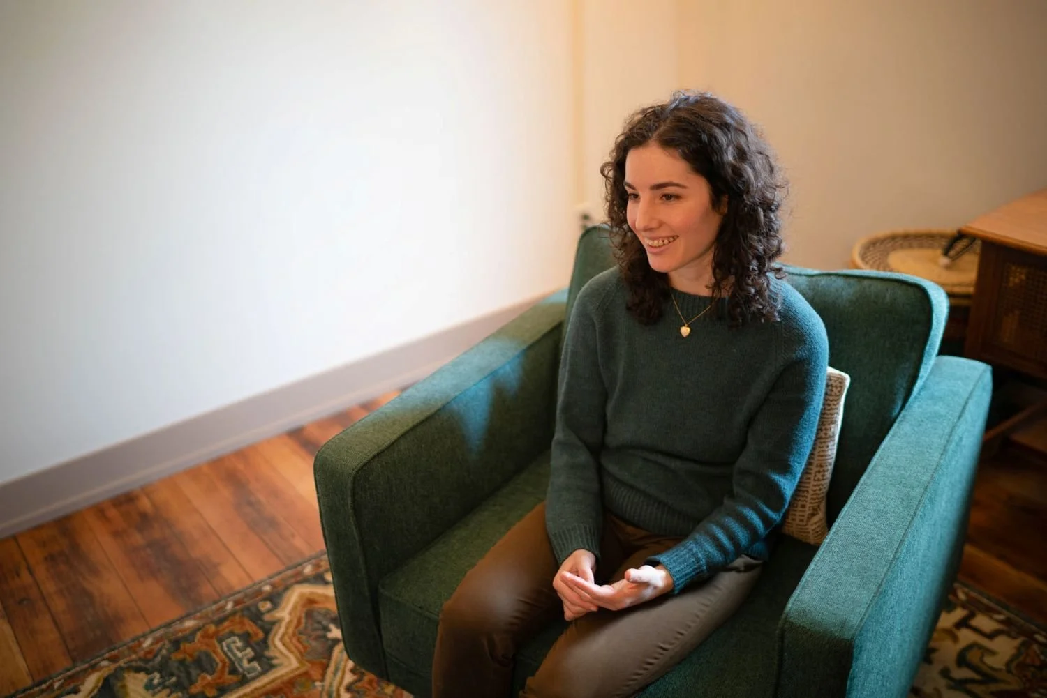 Vanessa seated in a green armchair in her office, hands open, mid-conversation.
