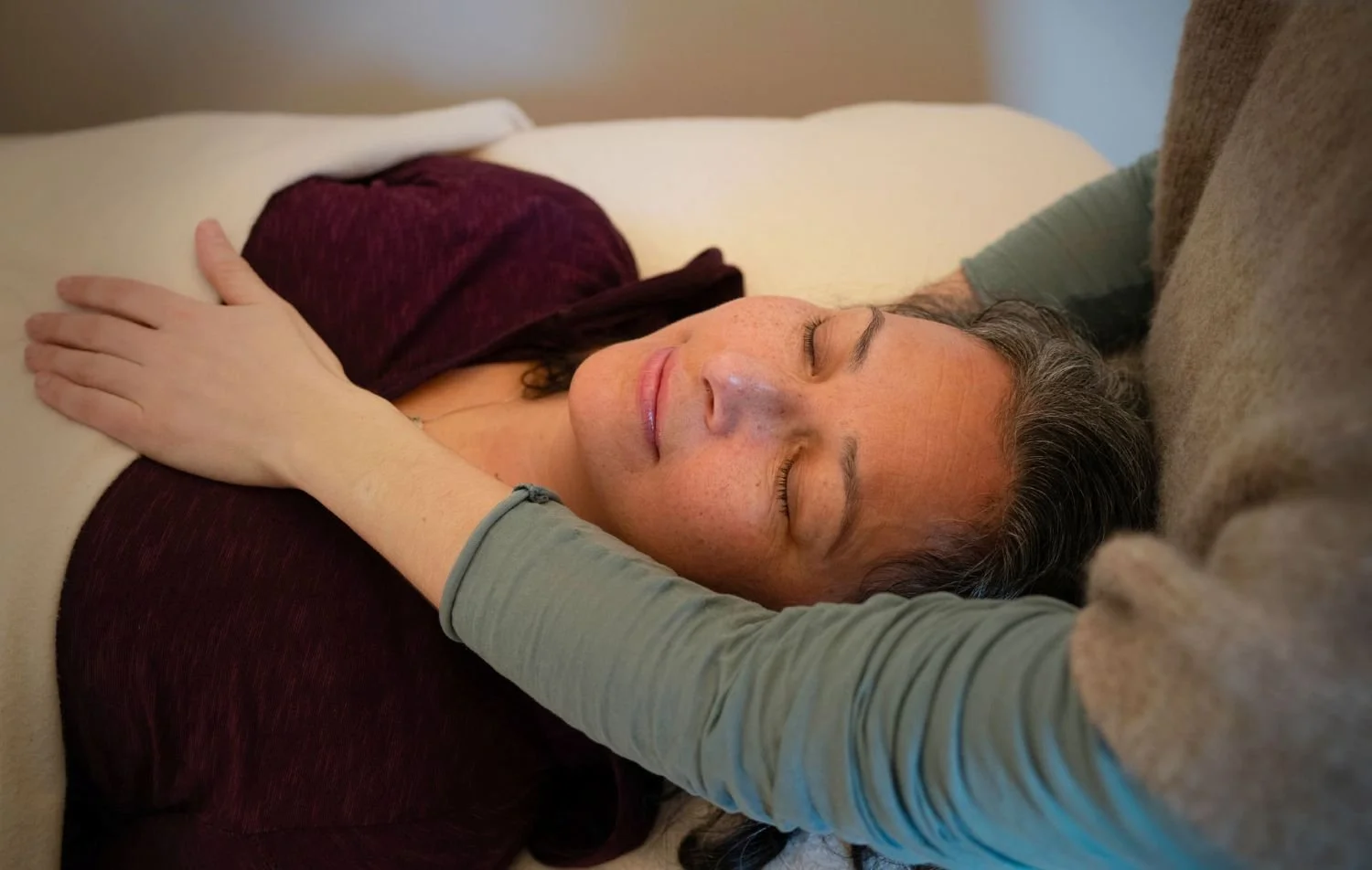 A client resting with eyes closed during a craniosacral session, Vanessa's hand placed on her heart.